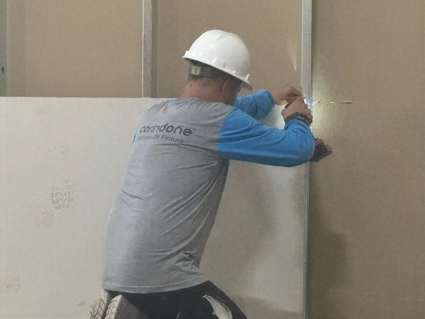 Profissional de capacete e camisa da Corindone fixando placa de drywall