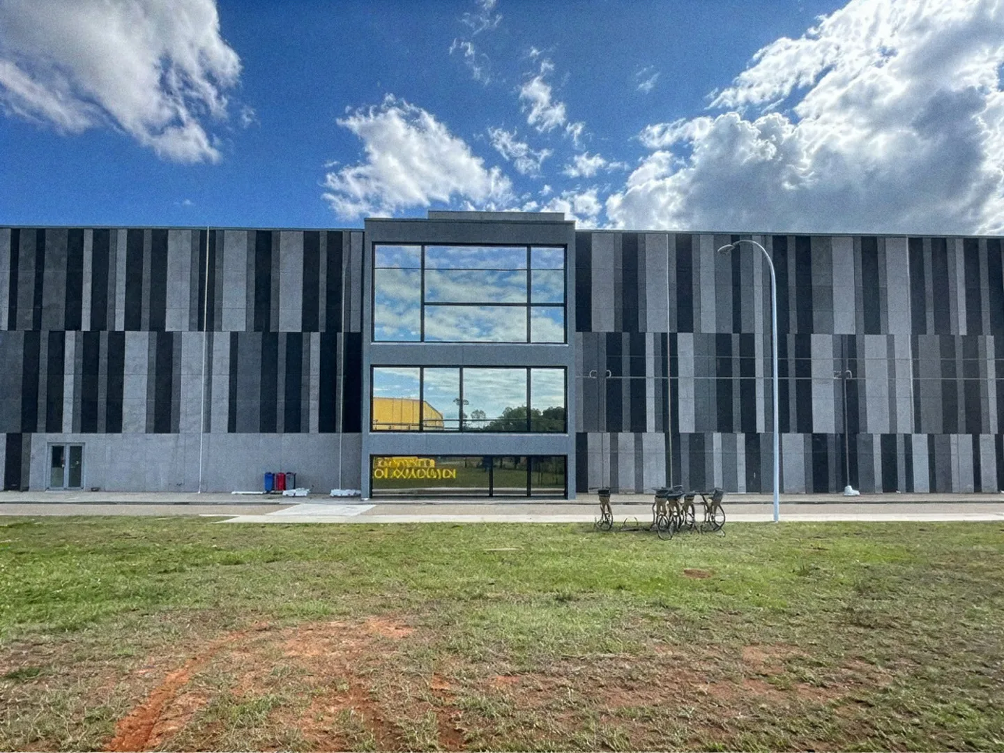 Prédio industrial de dois andares com fachada de painéis cinza e vidro, sob céu azul
